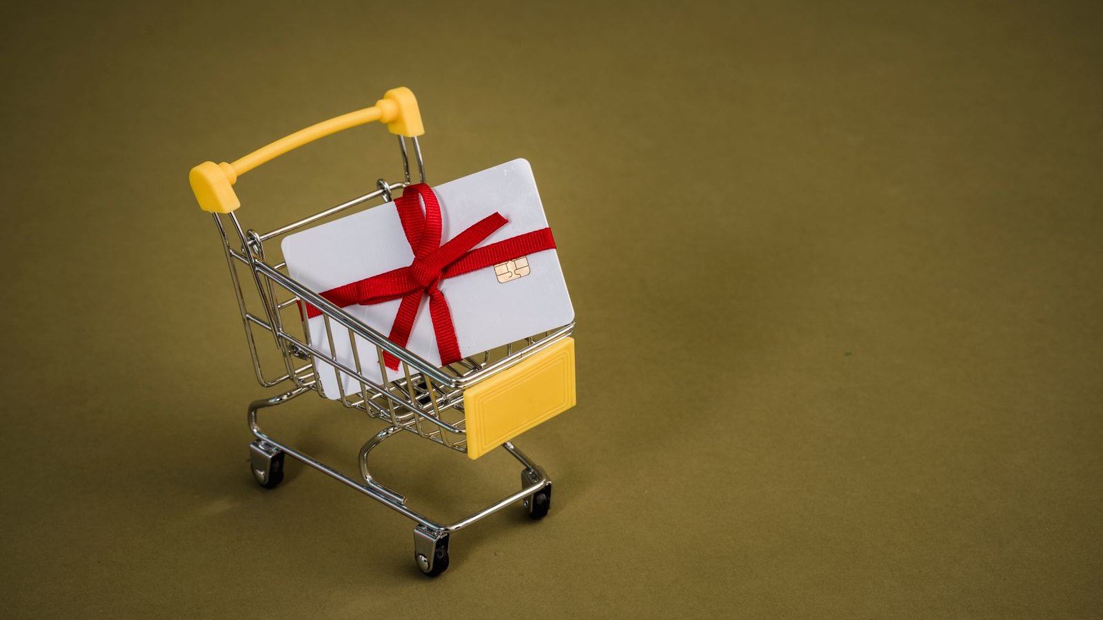 Bon podarunkowy z czerwoną kokardą w miniaturowym wózku na zakupy